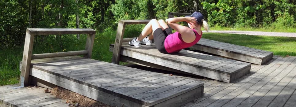En kvinna iklädd träningskläder gör situps vid en träningsbänk.