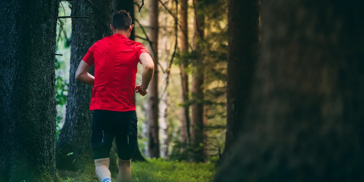 En man springer genom en skog i en röd skjorta.
