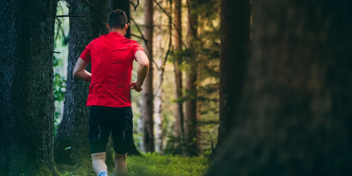 En man springer genom en skog i en röd skjorta.