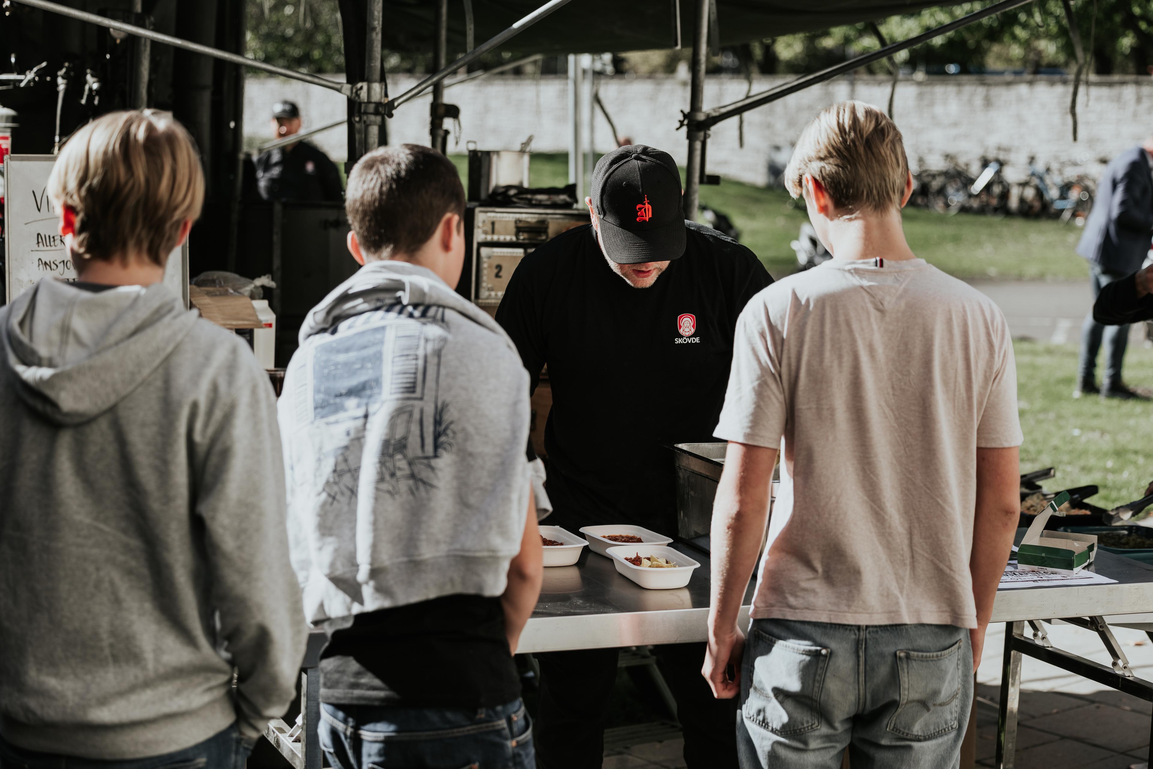 Tre ungdomar serveras mat utomhus