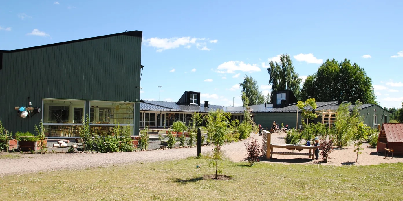 En grön byggnad med många träd framför sig